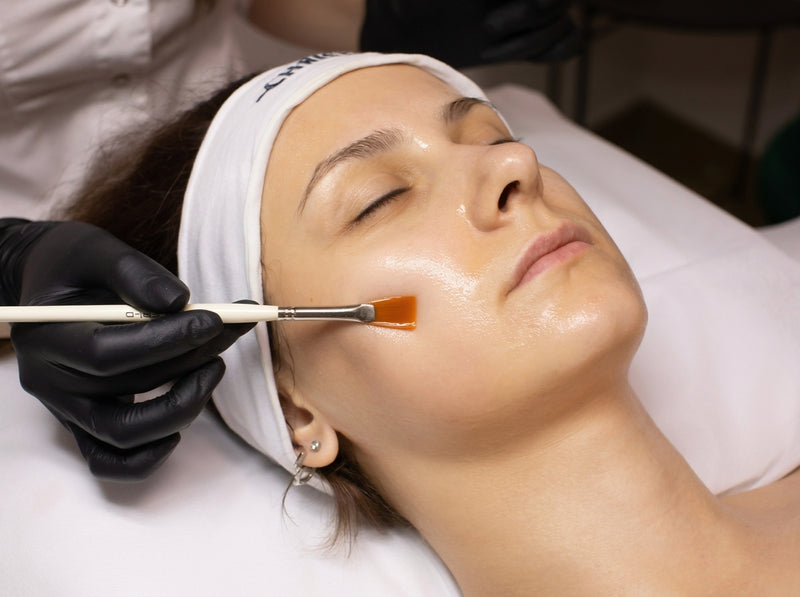 A woman having a facial mask brushed onto her skin