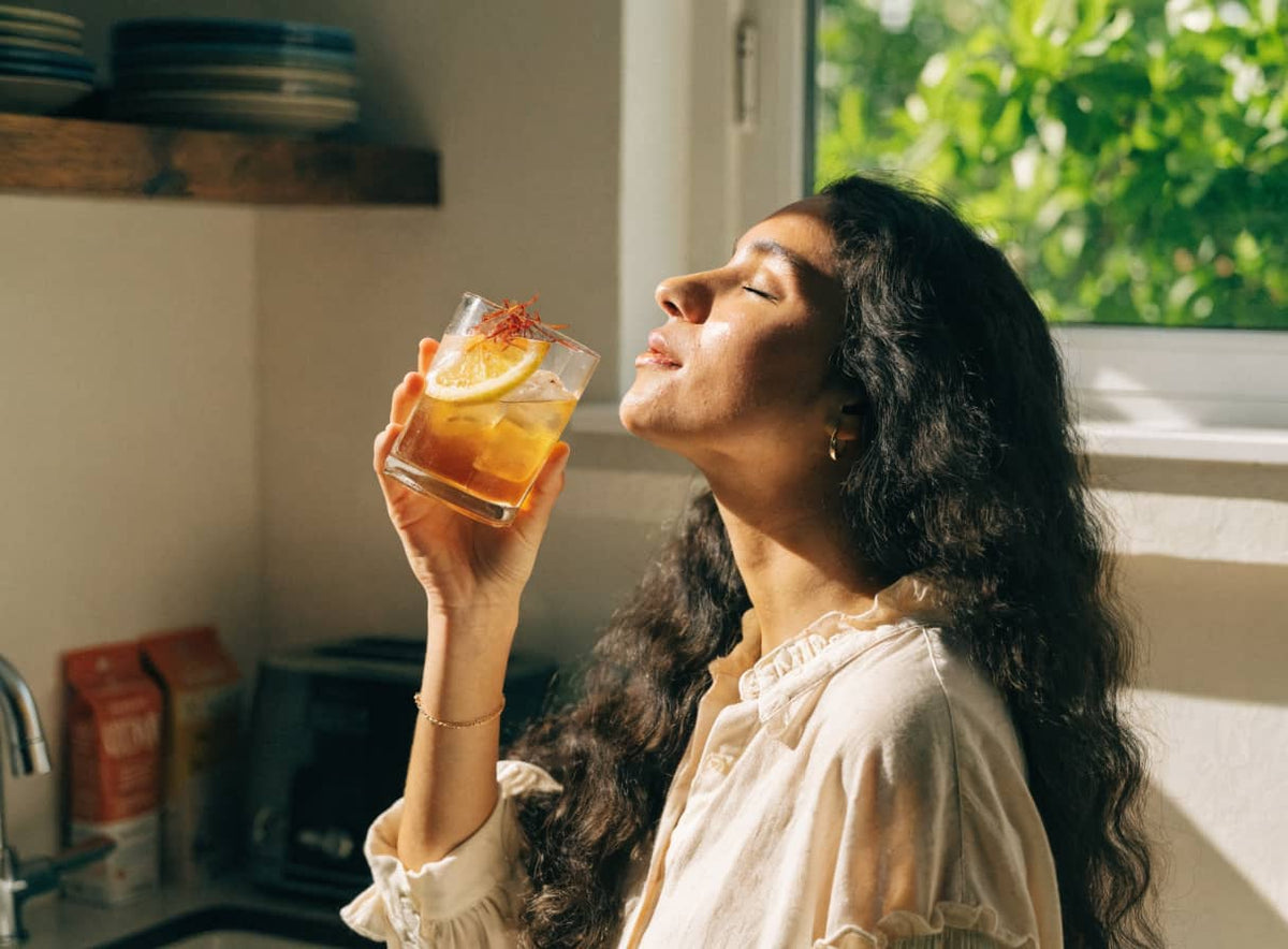 A woman sipping a drink in a sunny kitchen