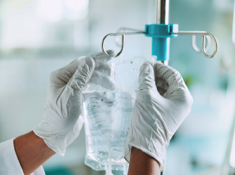 A gloved hand holding an IV bag