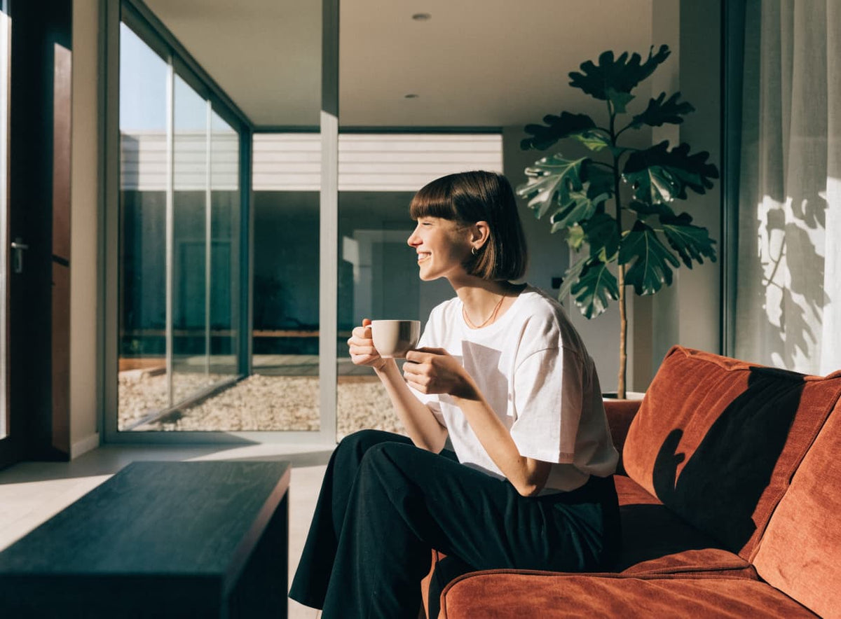 A woman relaxing on a sofa with a cup of coffee by a window