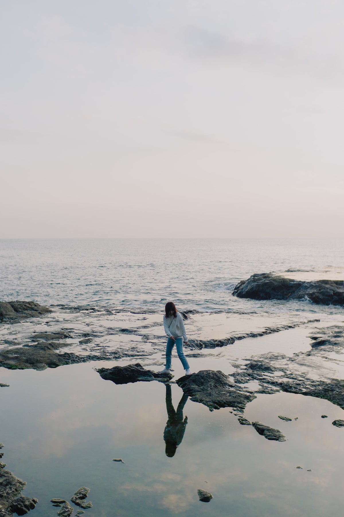 A person standing on rocks at the edge of the ocean at dusk