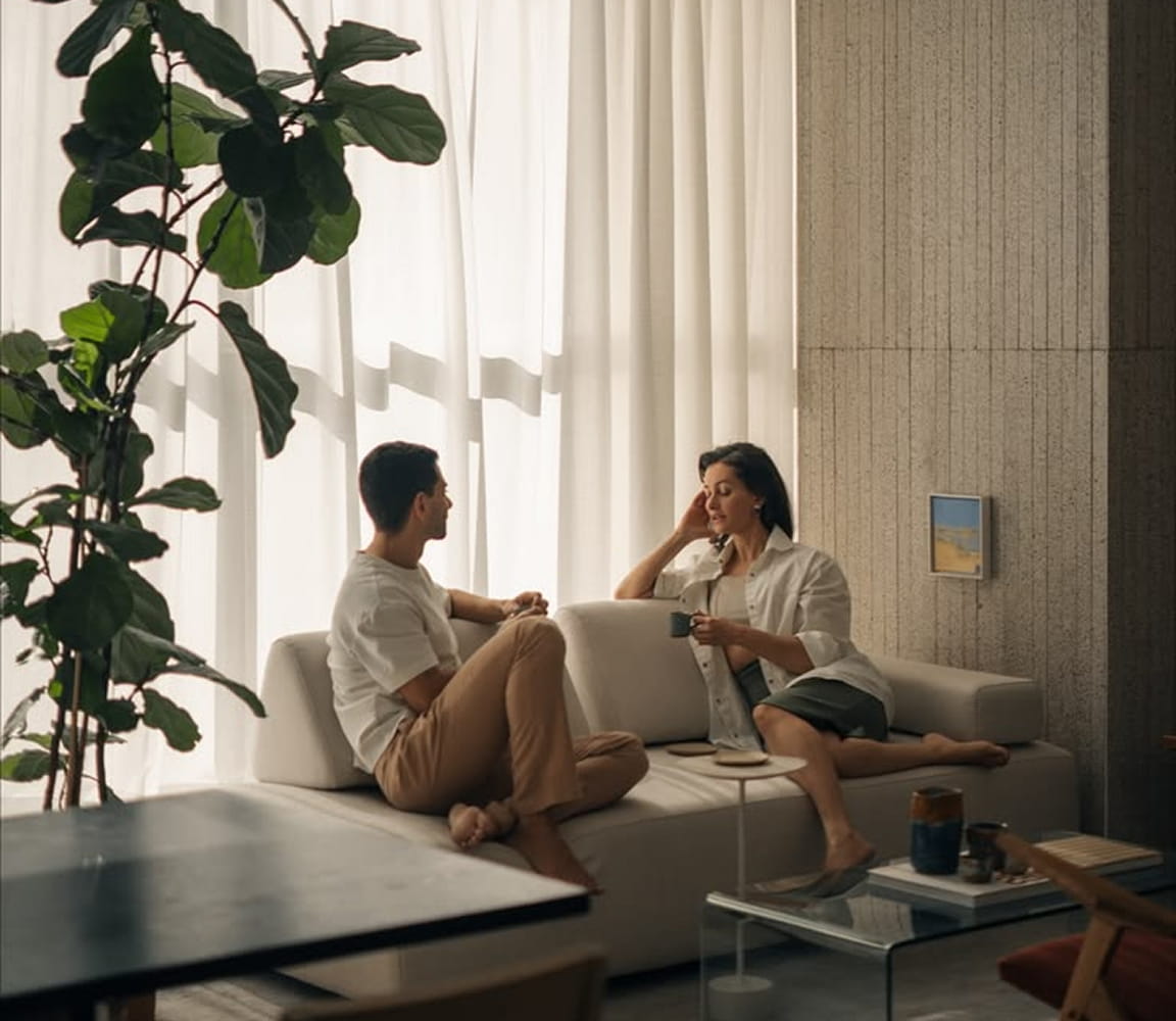 Two people talking on a sofa in a bright room with plants